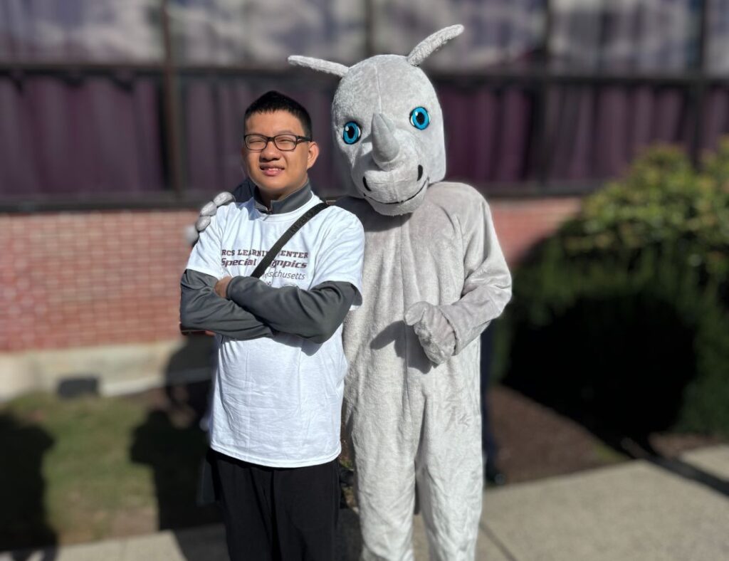 Teenage RCS Learning Center student posing next to school mascot, Riley the Rhino